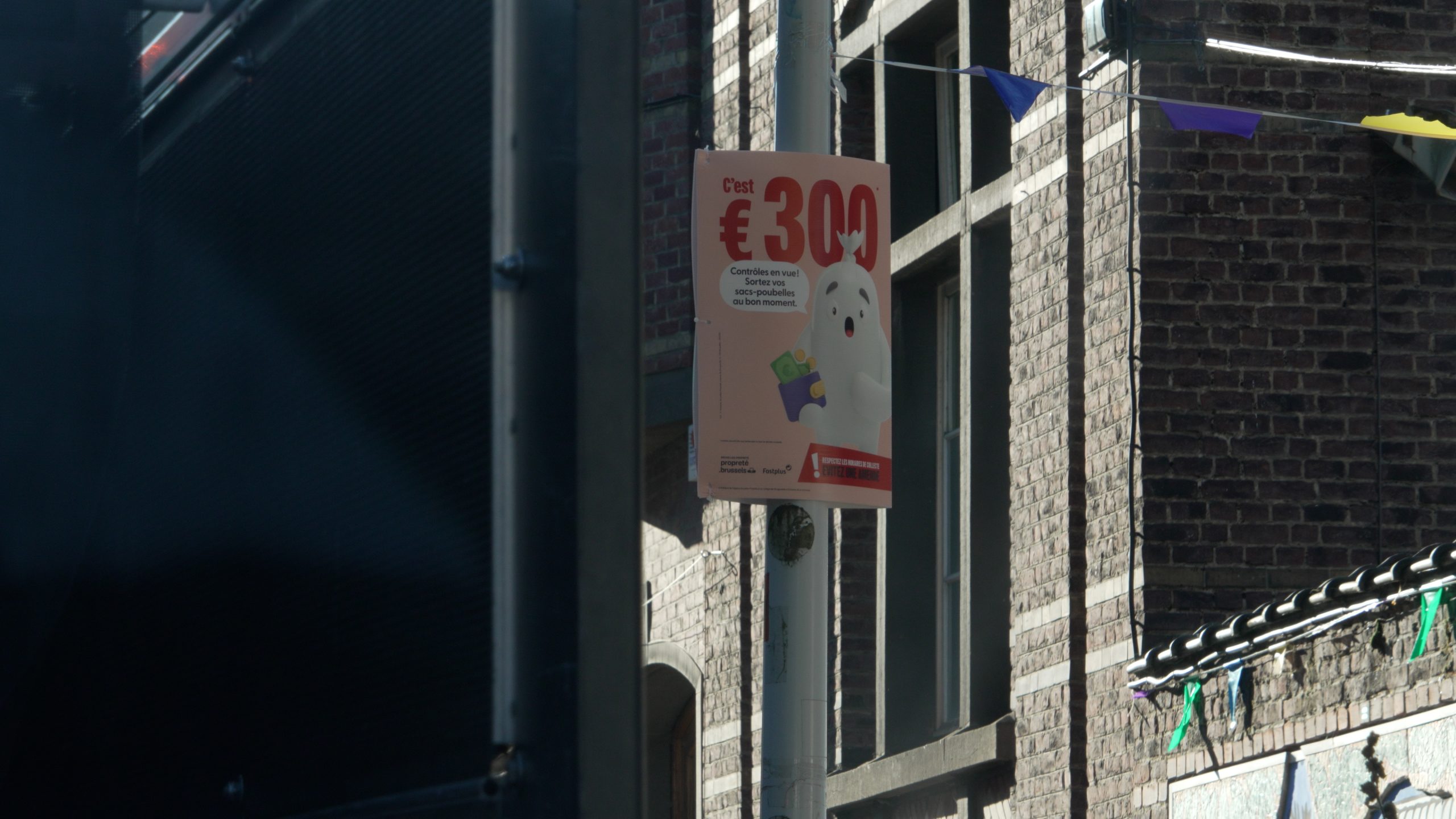 A €300 warning poster for illegal dumping attached to a pole on a Brussels street.