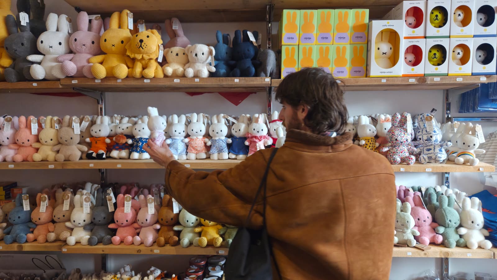 Man reaching for a Nijntje plush toy from a shelf inside a Nijntje store in Utrecht.