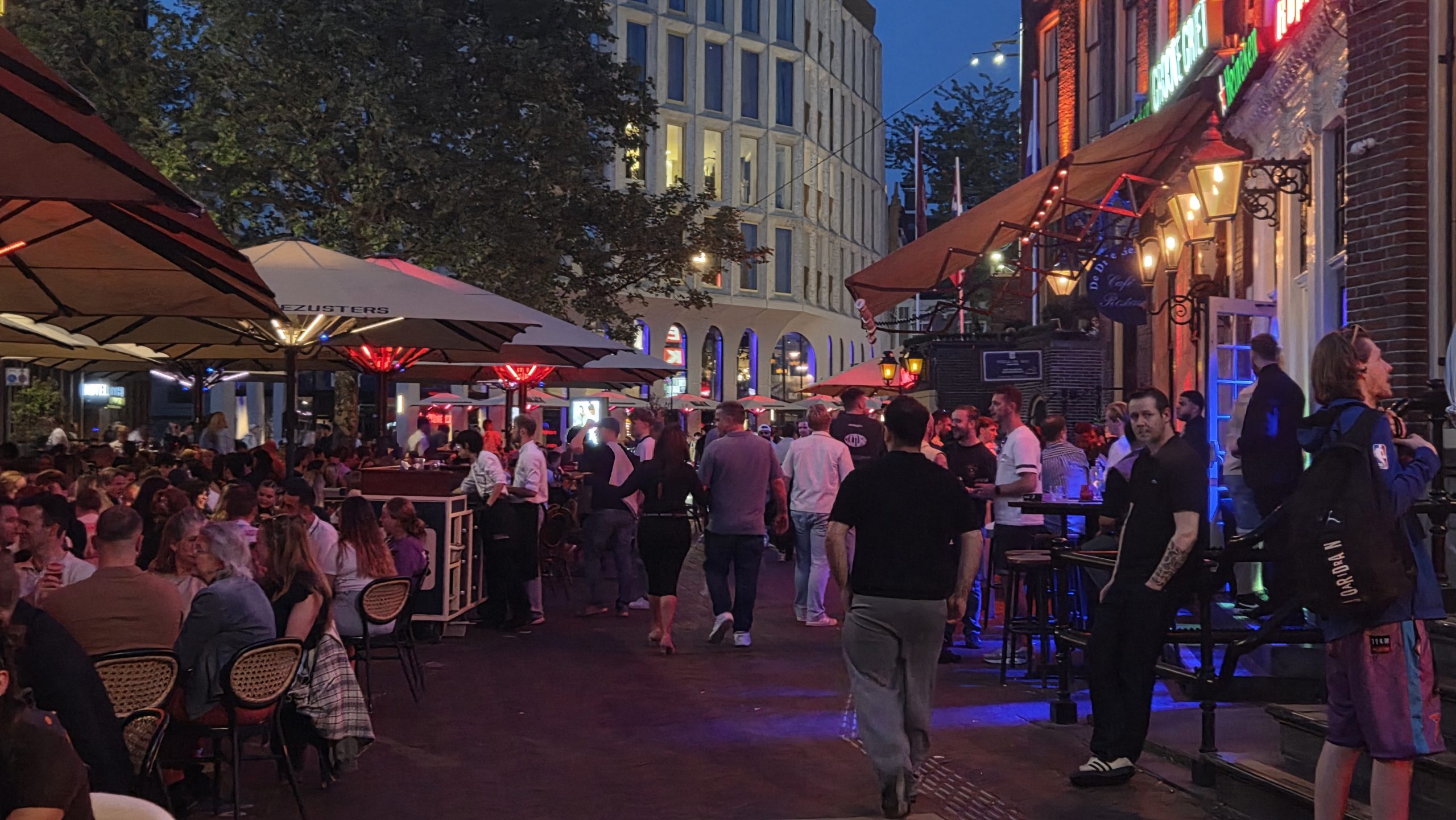 Crowded terraces and bars in Groningen at night, with many people sitting and standing under illuminated umbrellas.