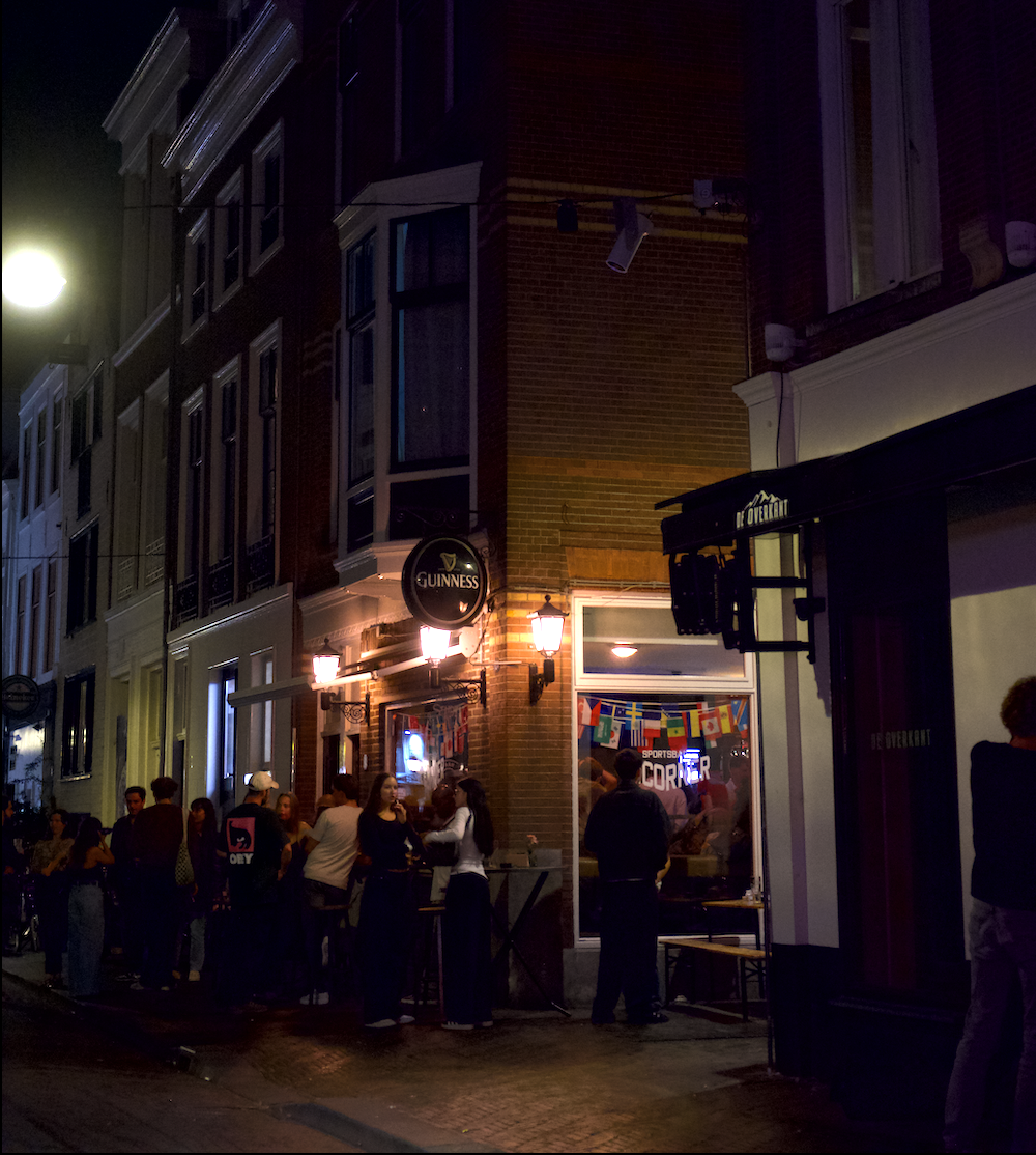 Herenstraat: Microphone and Projector with young people gathering outside a bar